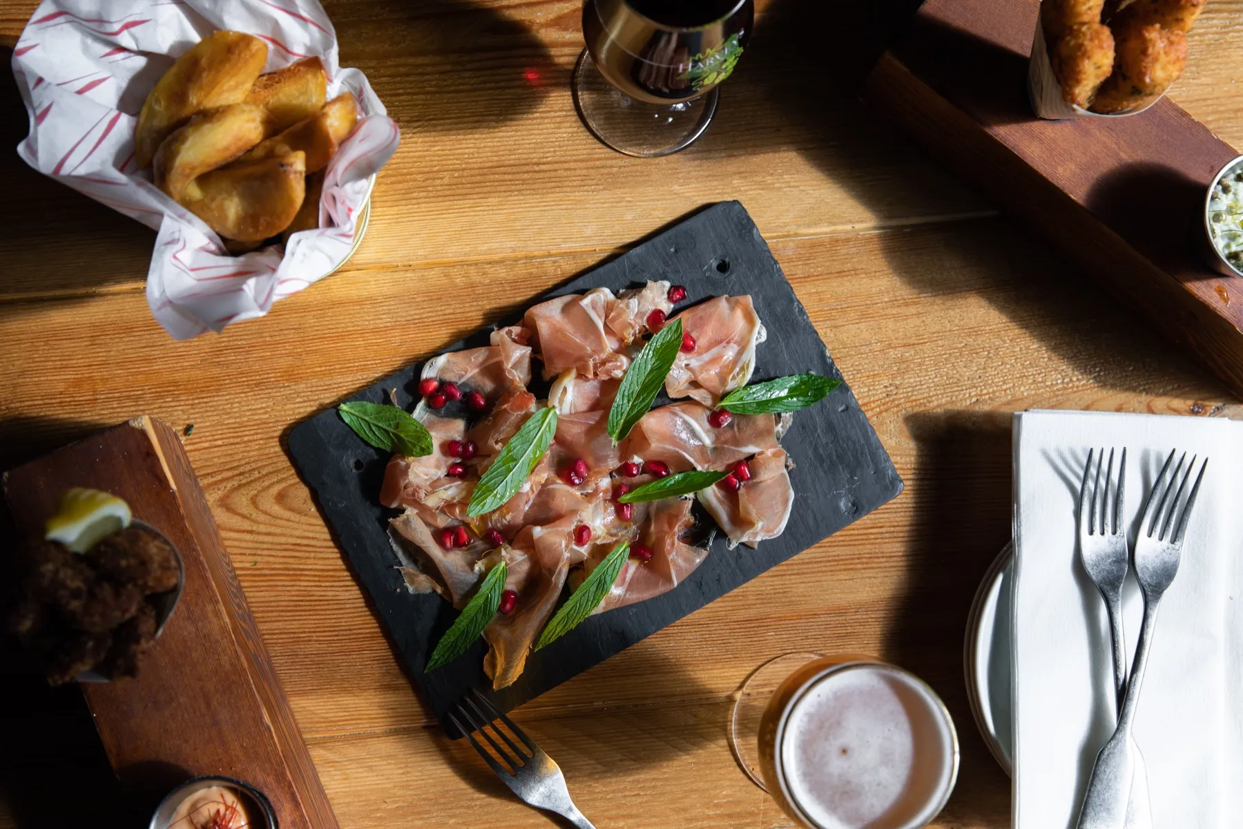 A slate of cured ham with pomegranate and a glass of beer